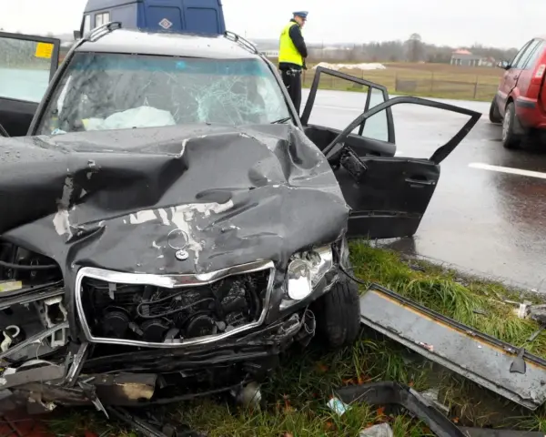 Zniszczony czarny samochód po wypadku, z otwartymi drzwiami i poobijanym przodem. Policjant stoi obok. Zastanawiasz się, ile wzrasta OC po szkodzie?
