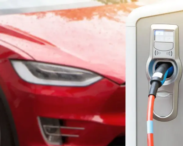 Czerwona Tesla podłączona do ładowarki. Zastanawiasz się, ile ładuje się Tesla? Czas ładowania zależy od modelu i mocy ładowarki.