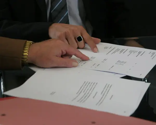Dwóch mężczyzn analizuje dokumenty, jeden wskazuje palcem na tekst. Może to być wypowiedzenie umowy AC.