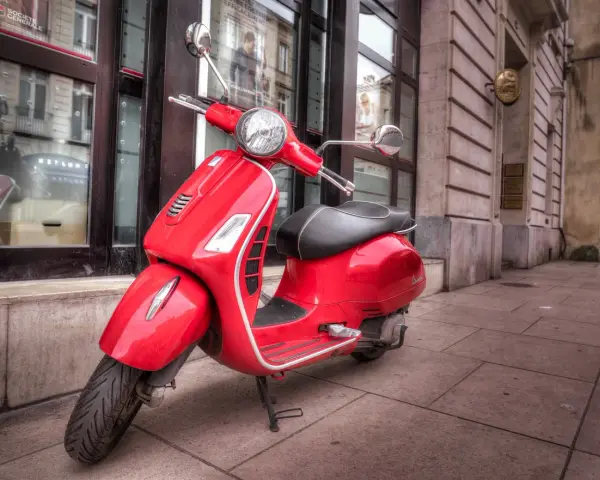 Czerwony skuter Vespa na chodniku. Zastanawiasz się, od ilu lat można jeździć motorowerem?