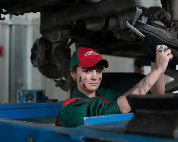 Mechaniczka z plamami smaru na twarzy pracuje pod samochodem, oferując fachową assistance midi.