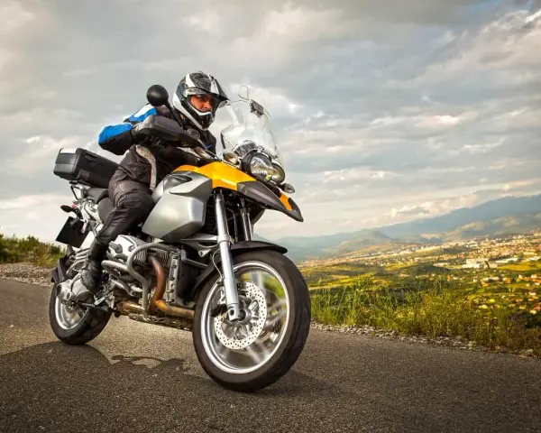 Motocyklista w kasku i kurtce jedzie drogą z widokiem na miasto w oddali. To może być początek jego przygody z rejestracją motocykla z zagranicy.