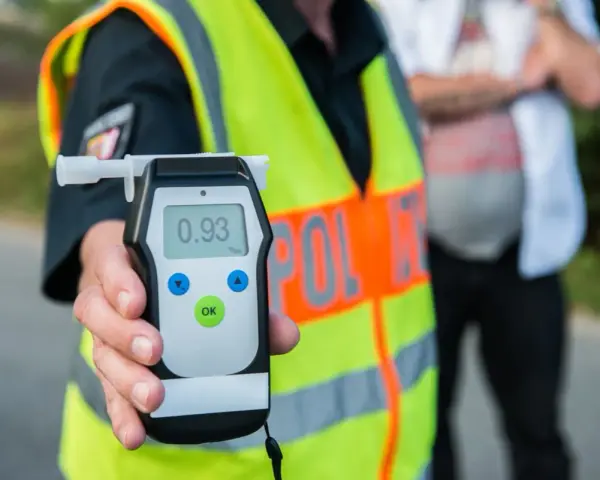 Policjant w kamizelce odblaskowej pokazuje alkomat z wynikiem 0.93 promila. Rutynowa kontrola trzeźwości na drodze.