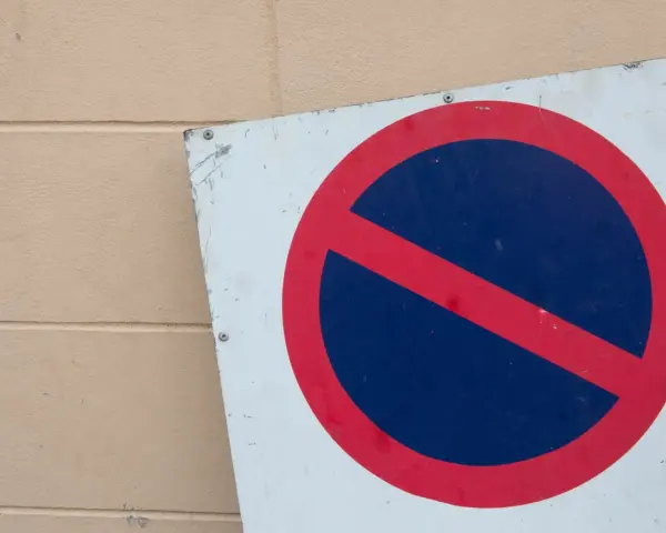 Znak zakaz postoju na białym tle, z czerwonym okręgiem i przekreśleniem na niebieskim tle.