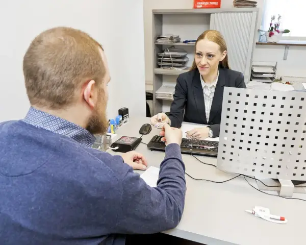 Mężczyzna przekazuje dokument urzędniczce, kiedy wymiana prawa jazdy jest w toku.