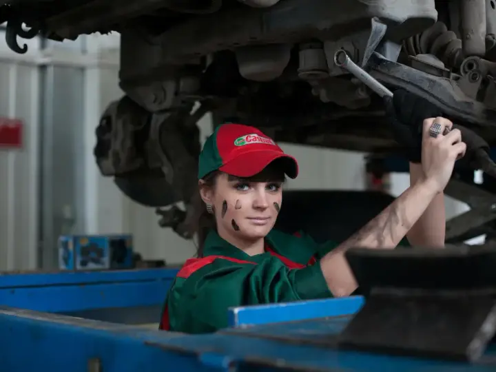 Mechaniczka z plamami smaru na twarzy pracuje pod samochodem, oferując fachową assistance midi.