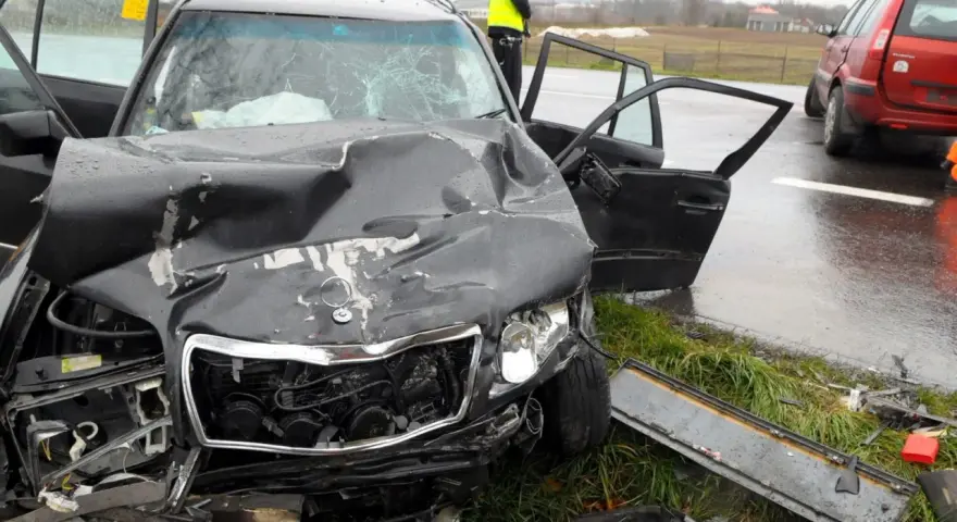 Zniszczony czarny samochód po wypadku, z otwartymi drzwiami i poobijanym przodem. Policjant stoi obok. Zastanawiasz się, ile wzrasta OC po szkodzie?