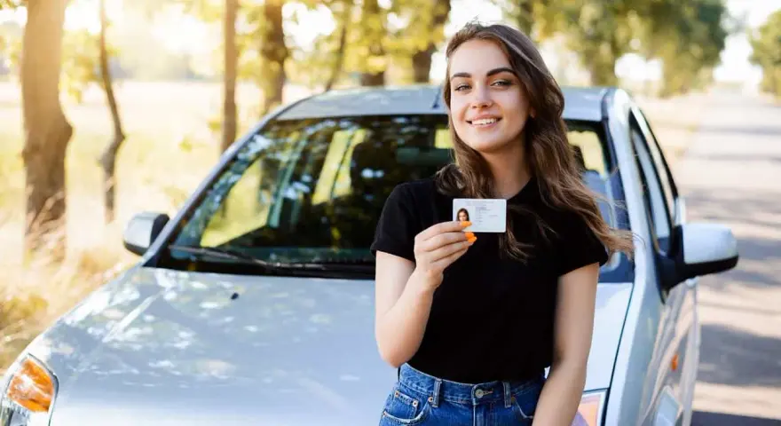 Szczęśliwa młoda kobieta z prawem jazdy 16 lat stoi obok samochodu.