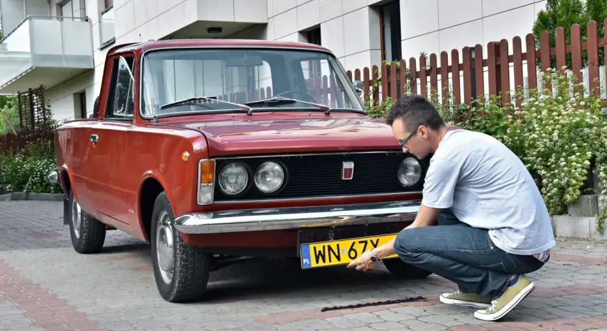 Mężczyzna montuje tablicę rejestracyjną do zabytkowego Fiata 125p. Proces ten jest kluczowy, by móc zarejestrować auto na zabytek.