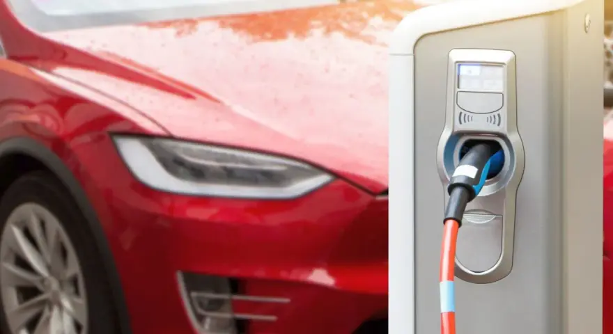 Czerwona Tesla podłączona do ładowarki. Zastanawiasz się, ile ładuje się Tesla? Czas ładowania zależy od modelu i mocy ładowarki.