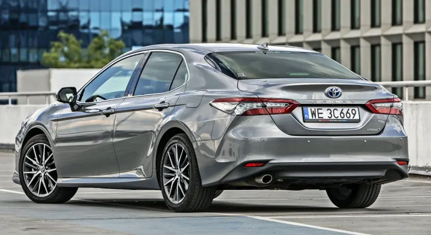 Szary sedan Toyota Camry Hybrid zaparkowany na parkingu. Sprawdź pojemność bagażnika tej hybrydy.