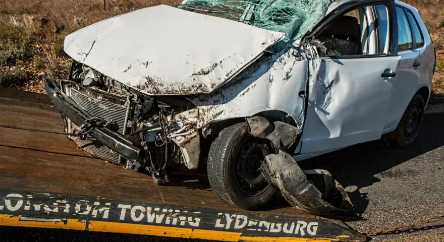 Biały samochód na lawecie z widocznymi uszkodzeniami, pęknięta przednia szyba. Wygląda na to, że to szkoda całkowita z OC sprawcy.