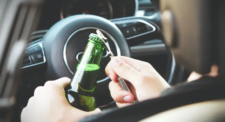 Ręce otwierają butelkę piwa za kierownicą. To niebezpieczna jazda pod wpływem alkoholu, która może skończyć się tragicznie.