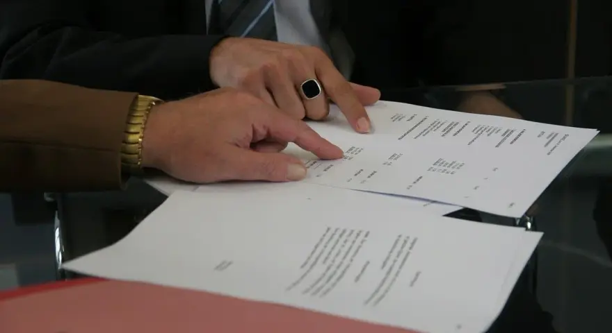 Dwóch mężczyzn analizuje dokumenty, jeden wskazuje palcem na tekst. Może to być wypowiedzenie umowy AC.