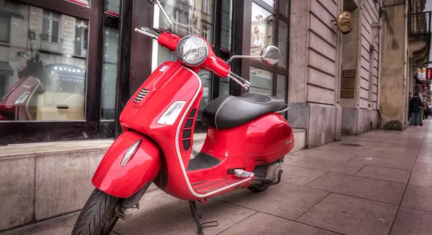 Czerwony skuter Vespa na chodniku. Zastanawiasz się, od ilu lat można jeździć motorowerem?