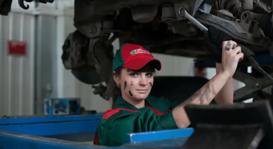 Mechaniczka z plamami smaru na twarzy pracuje pod samochodem, oferując fachową assistance midi.