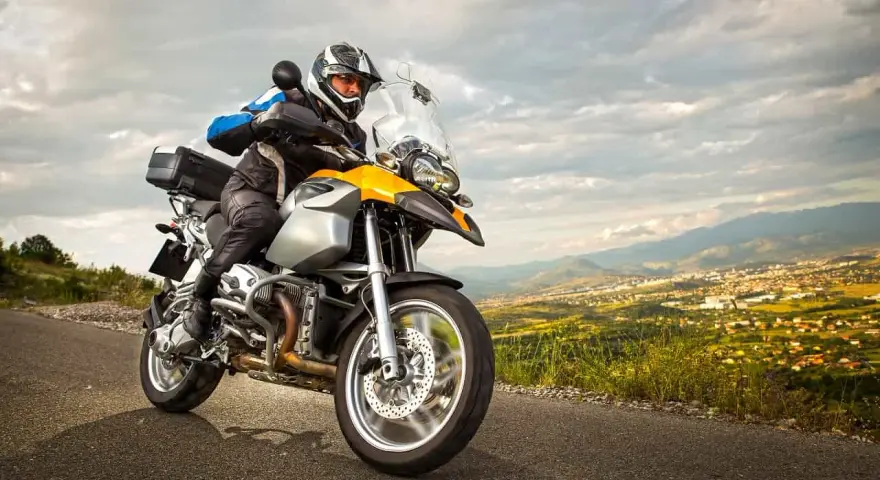 Motocyklista w kasku i kurtce jedzie drogą z widokiem na miasto w oddali. To może być początek jego przygody z rejestracją motocykla z zagranicy.