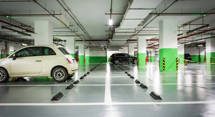 Jasny samochód i ciemny SUV na parkingu podziemnym. Widać odległość miejsca postojowego od ściany, zaznaczoną przez czarne odbojniki.