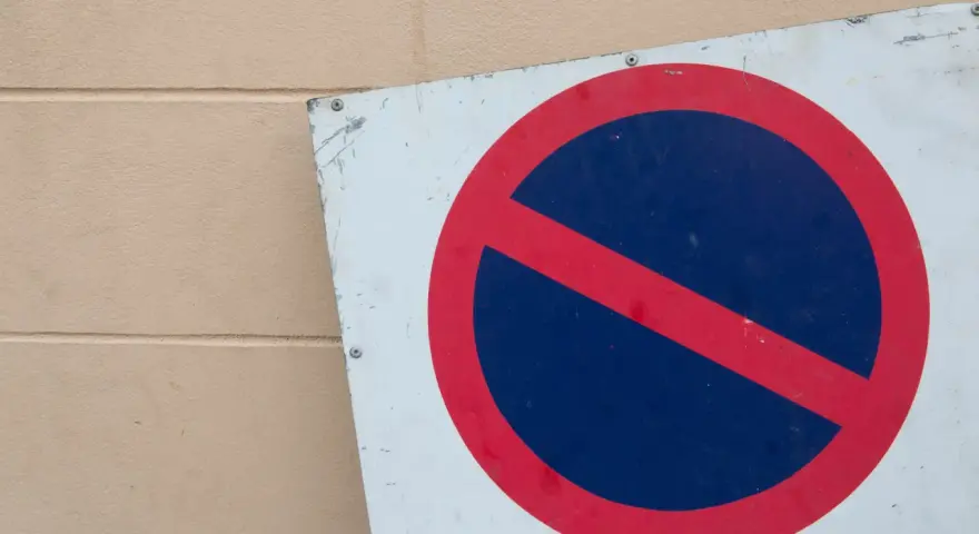 Znak zakaz postoju na białym tle, z czerwonym okręgiem i przekreśleniem na niebieskim tle.