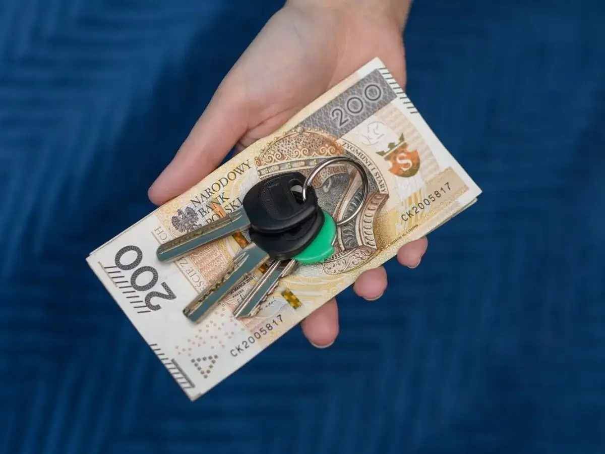 Dłoń trzyma banknot 200 zł i kluczyki do samochodu. To symbol zakupu lub sprzedaży auta, gdzie rejestracje samochodowe są kluczowe.