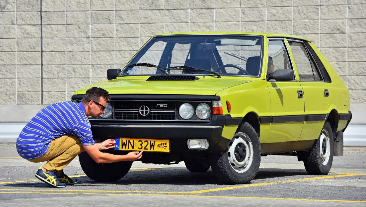 Mężczyzna przykręca żółtą tablicę rejestracyjną do zielonego Poloneza. To pierwszy krok, by zarejestrować auto na zabytek.