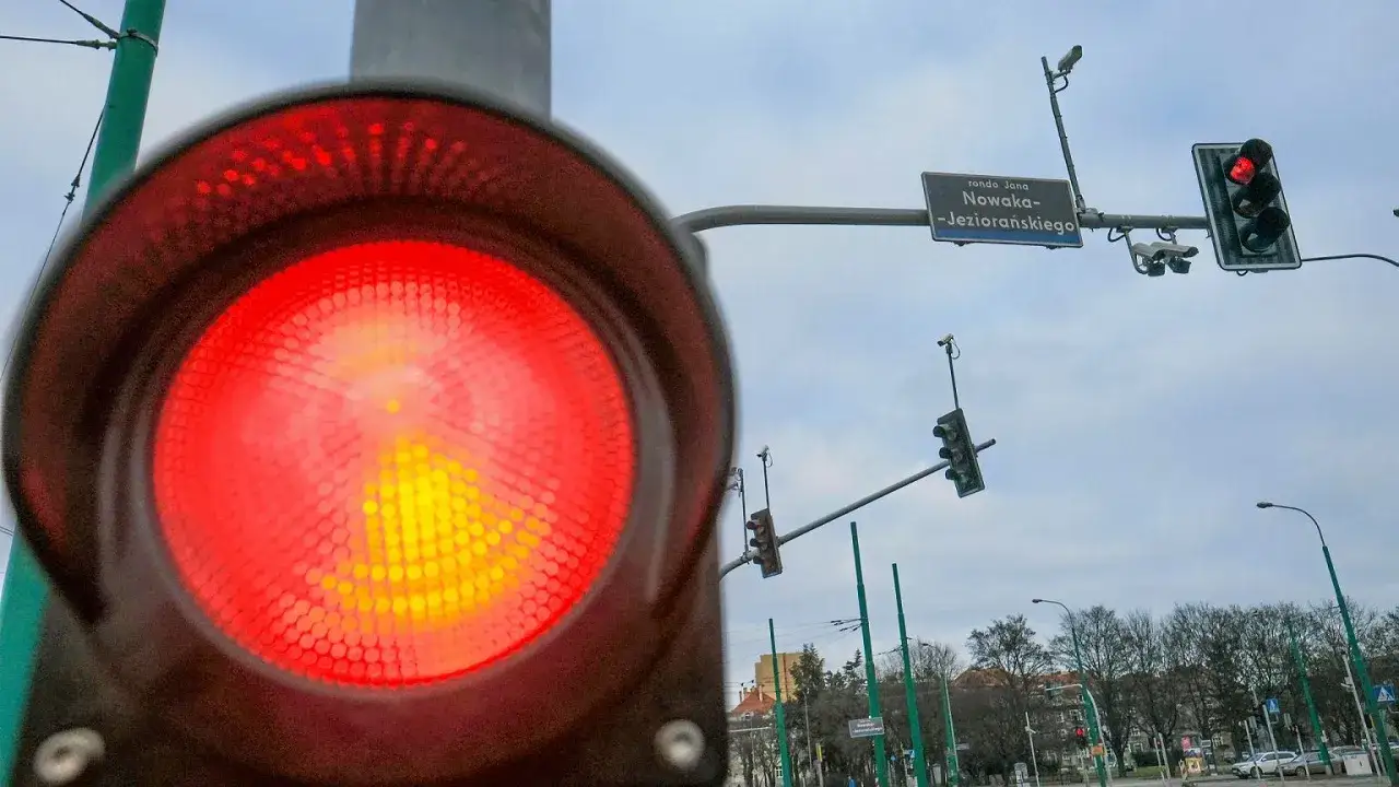 Czerwone światło sygnalizatora, znak ronda Jana Nowaka-Jeziorańskiego i kamery. Uważaj, by nie popełnić wykroczenia przejechanie na czerwonym świetle.
