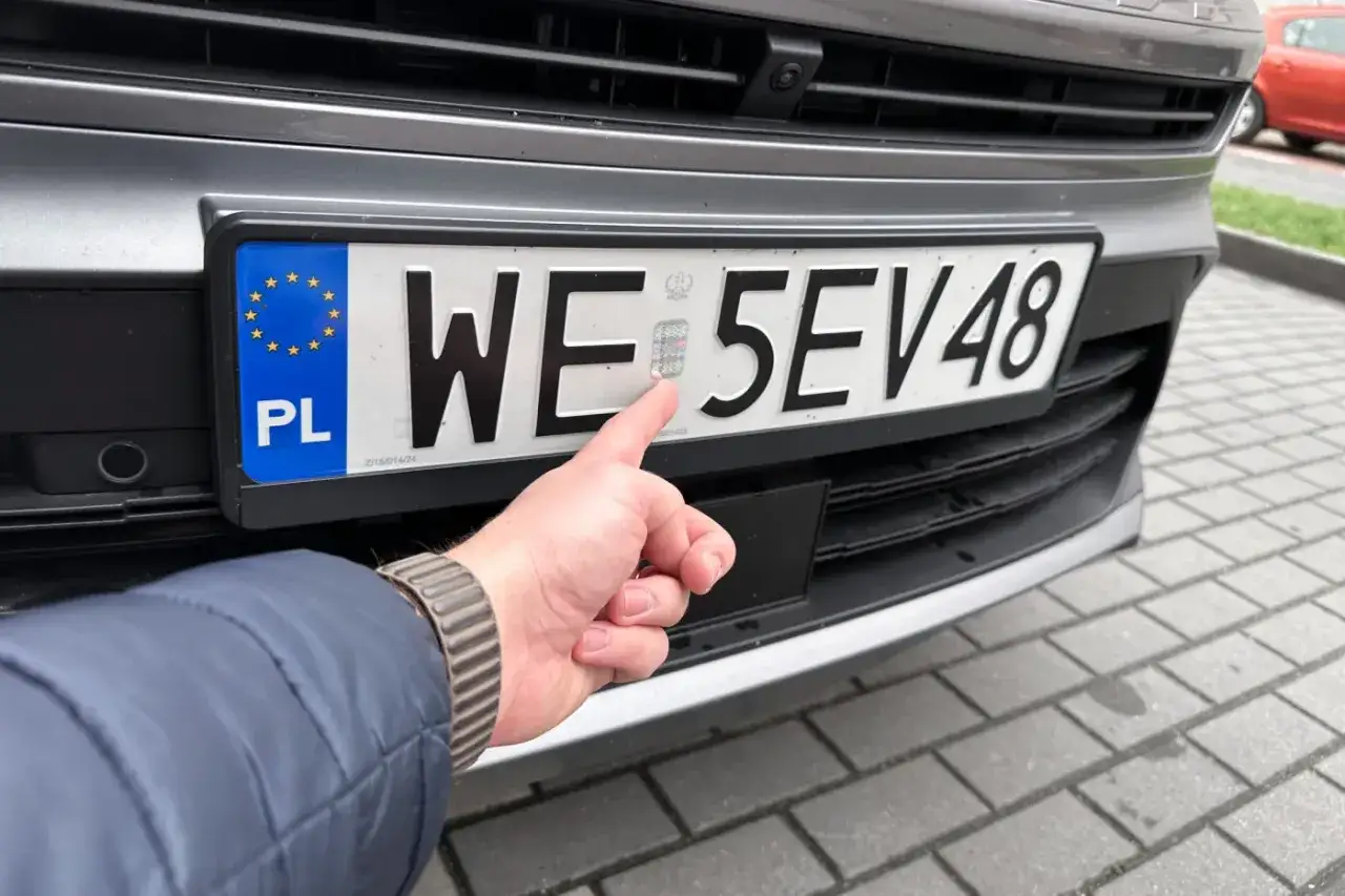 Palec wskazuje hologram na tablicy rejestracyjnej. Uniknij kary za nieprzerejestrowanie pojazdu, dbając o aktualność dokumentów.