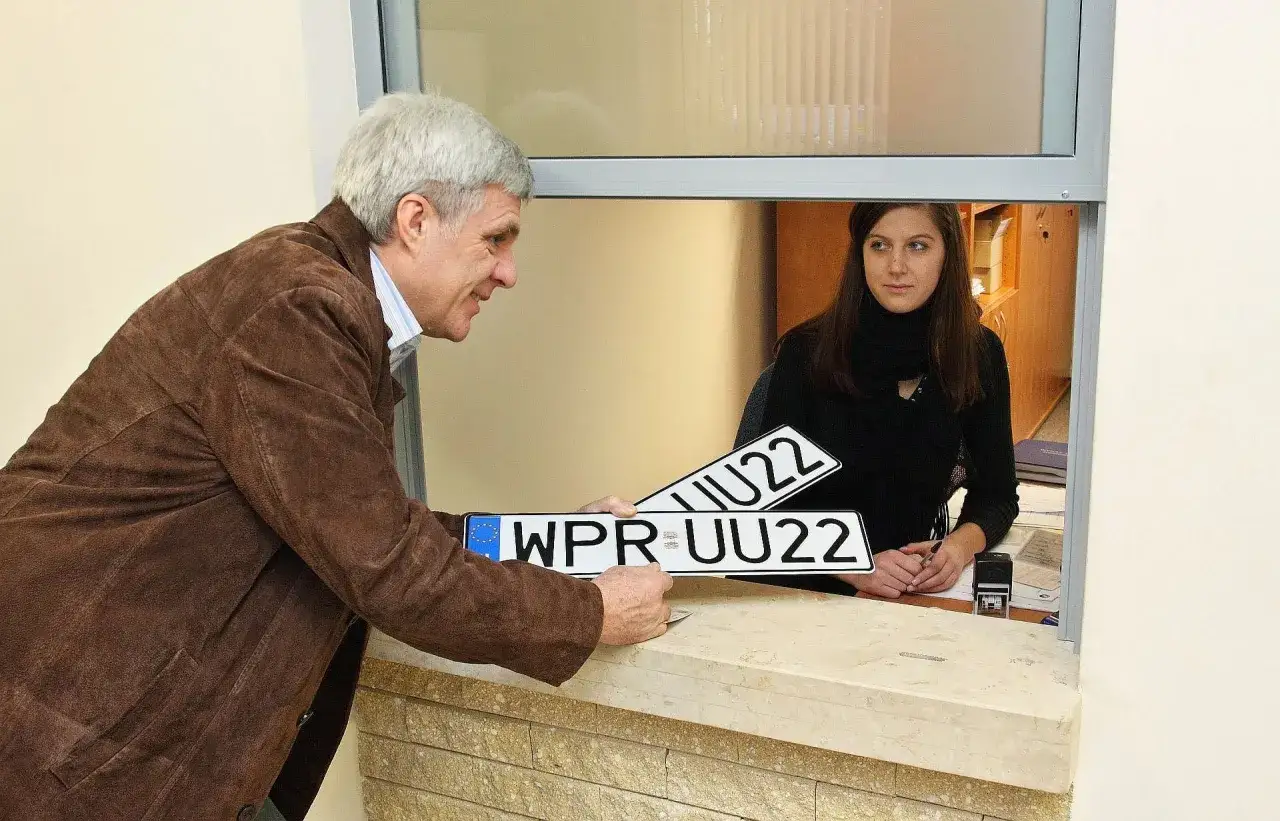 Mężczyzna przekazuje urzędniczce nowe tablice rejestracyjne do wymiany.