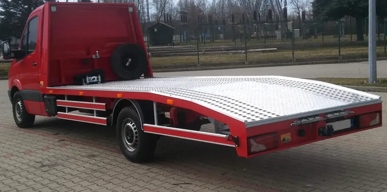 Czerwony laweta z platformą, gotowa do transportu. To właśnie co nazywamy zespołem pojazdów, gdy jeden służy do przewozu drugiego.