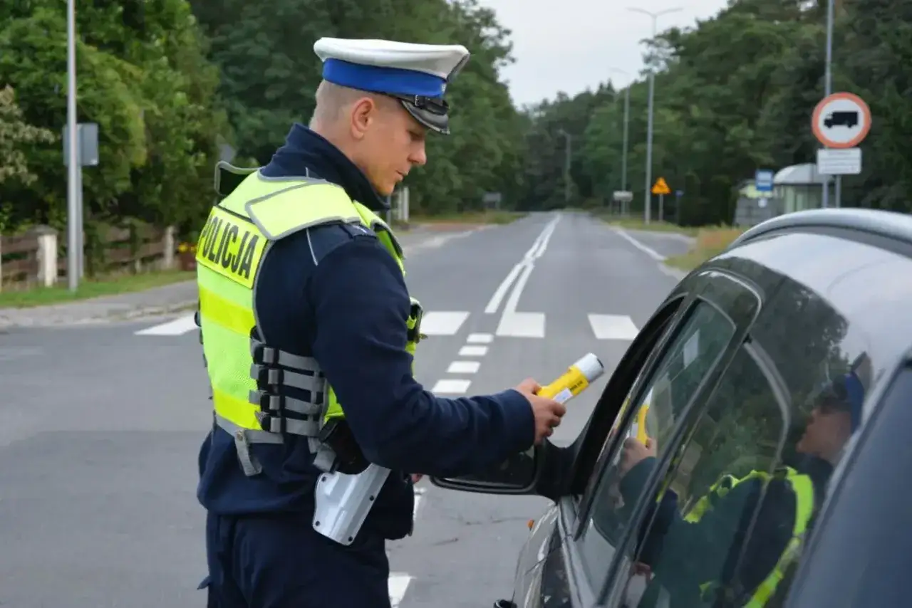 Policjant kontroluje kierowcę alkomatem. Pamiętaj, że kary za jazdę po alkoholu są surowe.