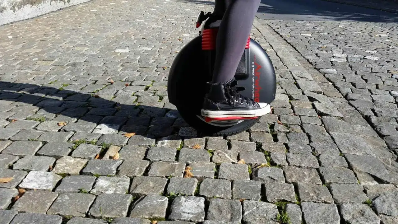 Osoba na monocyklu, jednym z nowoczesnych urządzeń transportu osobistego, pokonuje brukowaną ścieżkę.