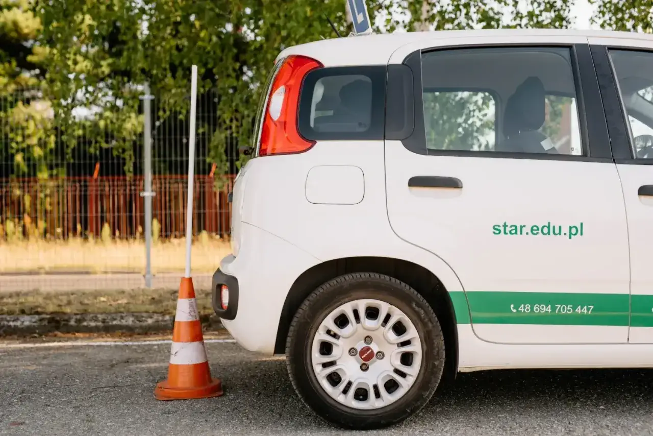 Biały samochód szkoleniowy z pachołkiem obok. Zastanawiasz się, ile teraz kosztuje prawo jazdy? Sprawdź ofertę na star.edu.pl.
