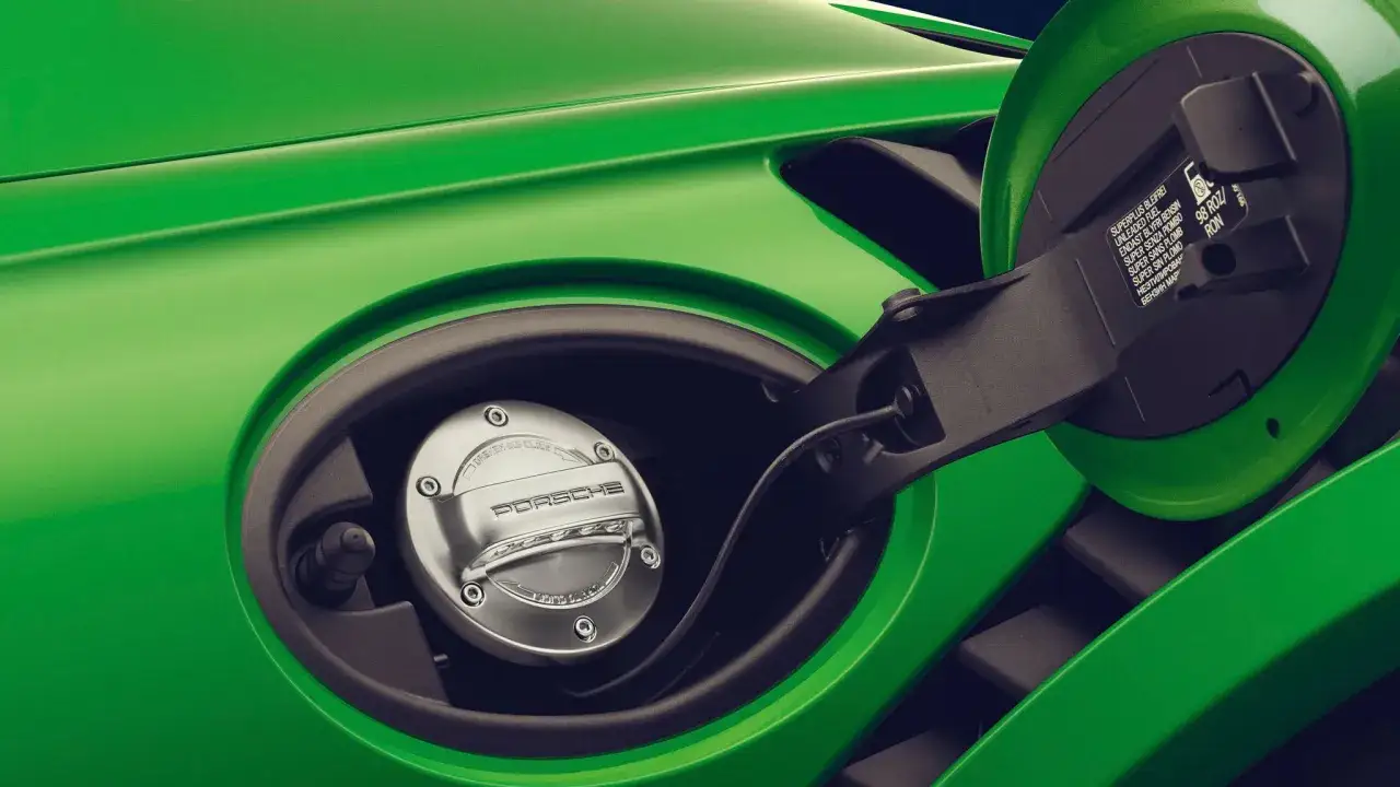 Zielony Porsche z otwartym wlewem paliwa. Wskazówka informuje o używaniu paliw syntetycznych, np. 98 RON.