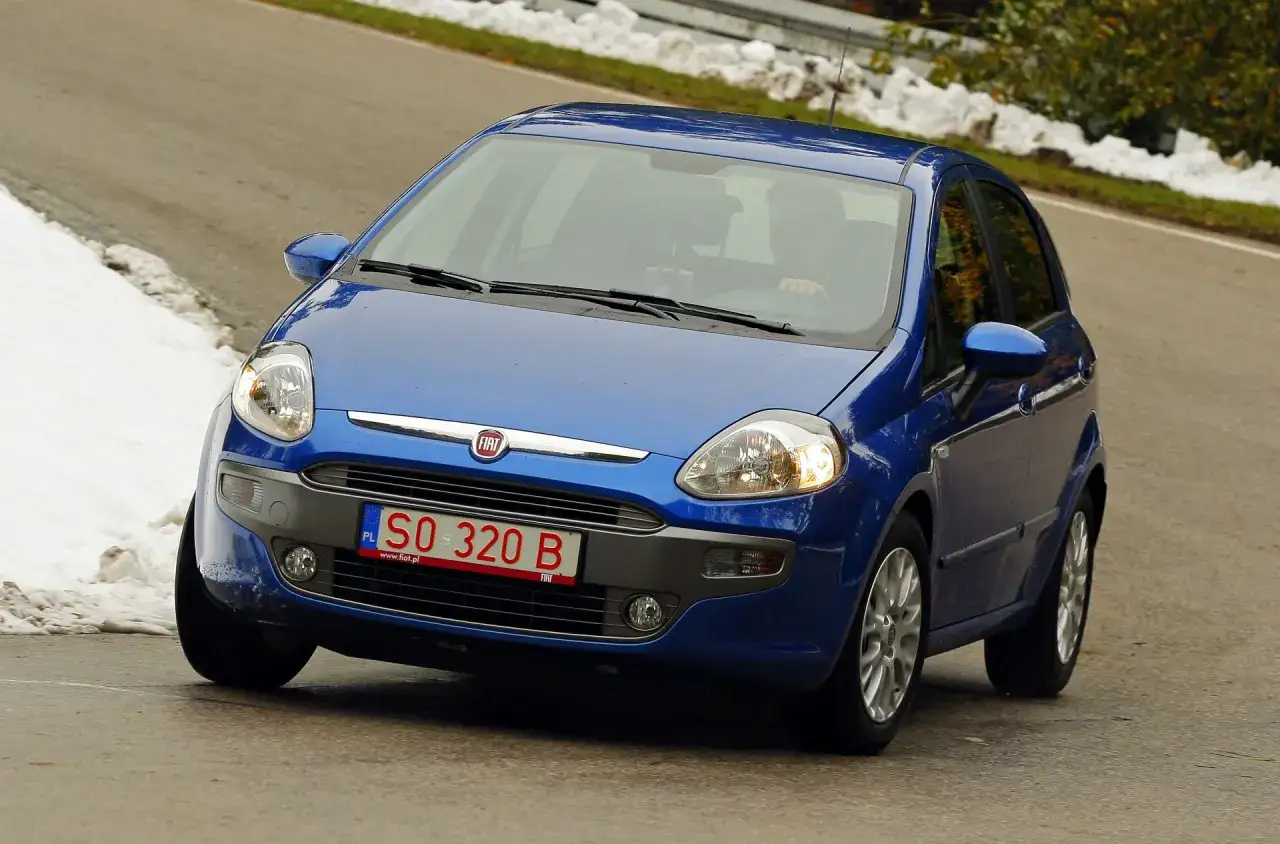Niebieski Fiat Punto z tymczasowymi tablicami rejestracyjnymi SO 320 B jedzie po krętej drodze z resztkami śniegu po bokach.