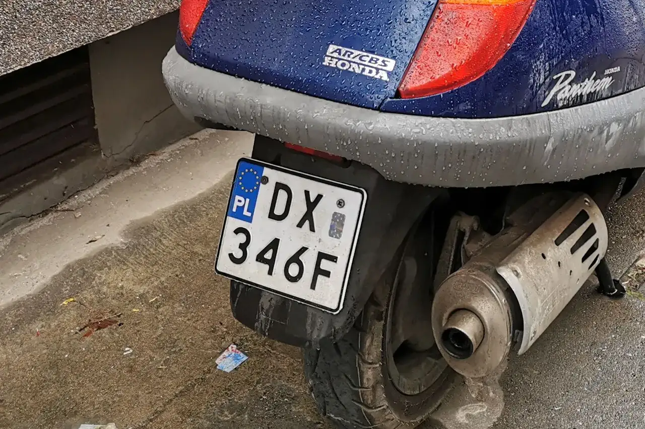 Niebieski skuter Honda Pantheon z tablicą rejestracyjną DX 346F stoi na mokrej nawierzchni.