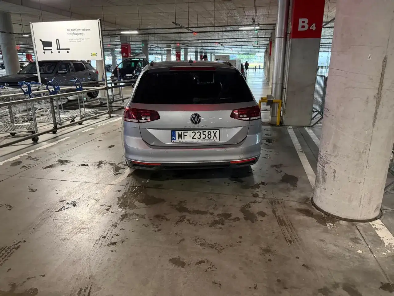 Srebrny Volkswagen na parkingu podziemnym. Tablica rejestracyjna WF 2358X. Obok wózek sklepowy.