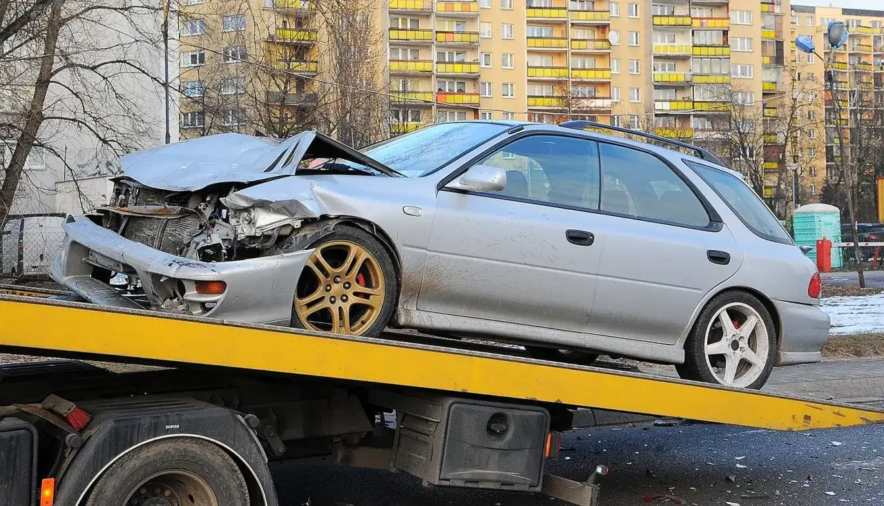Srebrne kombi z przodu mocno zniszczone, na lawecie. Wygląda na to, że czeka go szkoda całkowita a naprawa jest niemożliwa.