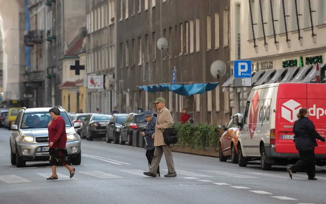 Ludzie przechodzą przez pasy, a obok stoi znak