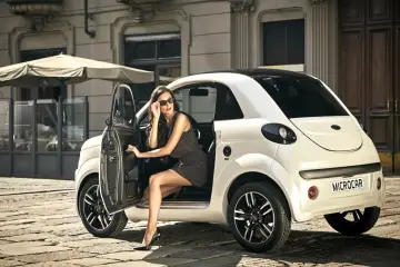 Elegancka kobieta w okularach przeciwsłonecznych wysiada z białego Microcara. Czy można zarejestrować samochód bez prawa jazdy?
