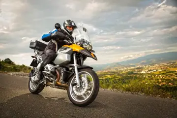 Motocyklista w kasku i kurtce jedzie drogą z widokiem na miasto w oddali. To może być początek jego przygody z rejestracją motocykla z zagranicy.