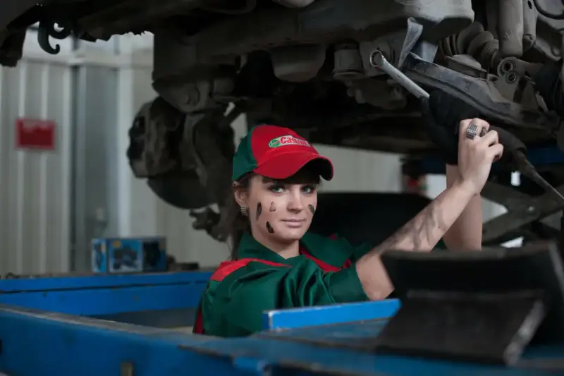 Mechaniczka z plamami smaru na twarzy pracuje pod samochodem, oferując fachową assistance midi.